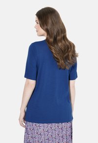 Tmavě modrý top s krátkým rukávem vyrobený z měkké látky, nošený přes sukni s květinovým vzorem. Top má volný střih a jednoduchý design.