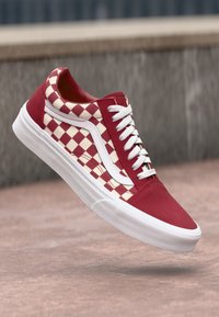 Vörös és krém árnyalatú sakktáblás alacsony szárú sneaker, fehér fűzőkkel és kiegészítőkkel, texturált panelek és gumitalp jellemzi.