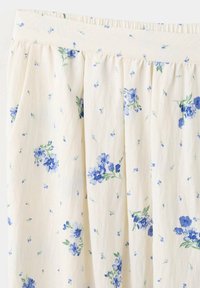 Jupe crème avec petit imprimé floral bleu et vert et taille froncée, montrant la texture du tissu et les détails du motif.