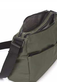 Bolsa de tela color verde oliva con múltiples compartimentos, cremalleras negras y una correa negra desmontable. Cuenta con un pequeño bolsillo frontal con cremallera.