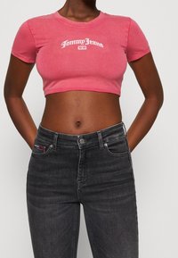 Růžové zkrácené tričko s bílým logem "Tommy Jeans", které je kombinováno s tmavě šedými džíny klasického střihu s jemným proužkováním na kapse.