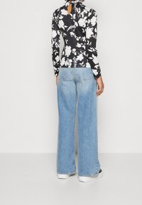 Zwart langmouwen top met witte bloemmotief, met een keyhole achterkant; gecombineerd met lichtblauwe wijde jeans en witte platform sneakers.