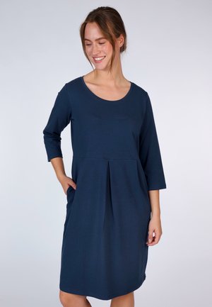 Kleid in Marineblau mit rundem Ausschnitt, dreiviertel Ärmeln, gefaltetem Vorderteil und seitlichen Taschen. Weicher Stoff mit lockerem Sitz.