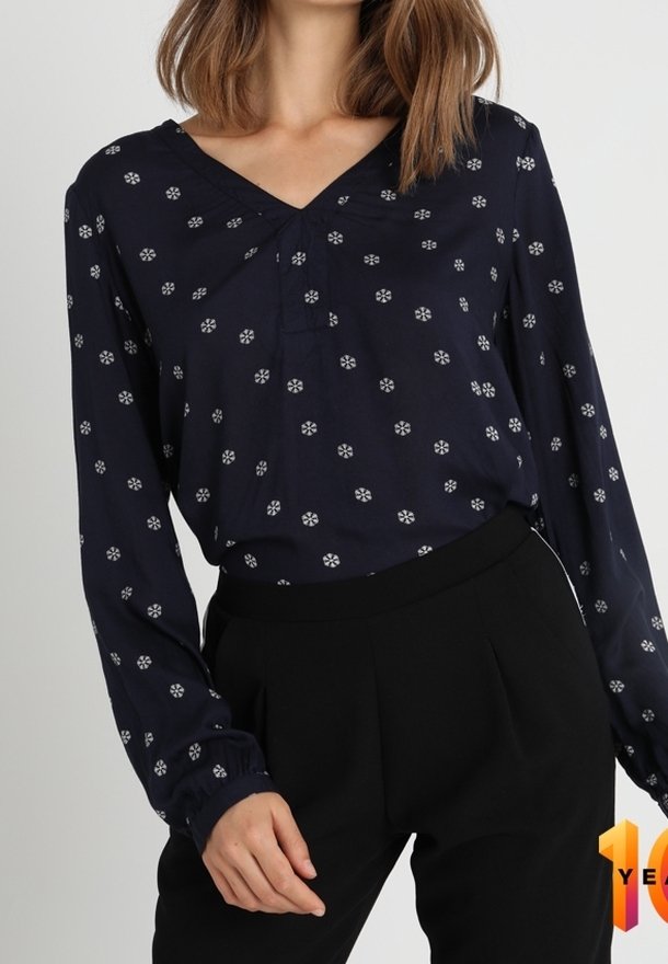 Blusa azul marino con patrón floral blanco, escote en V, mangas largas con puños fruncidos. Combinada con pantalones negros de cintura alta.