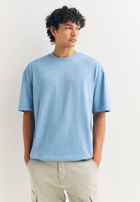 Hele sinine lühikeste varrukatega t-särk, valmistatud pehmest kangast, ümara kaelusega ja lõdva istuvusega, kombineeritud helebeežide cargo lühikestega.