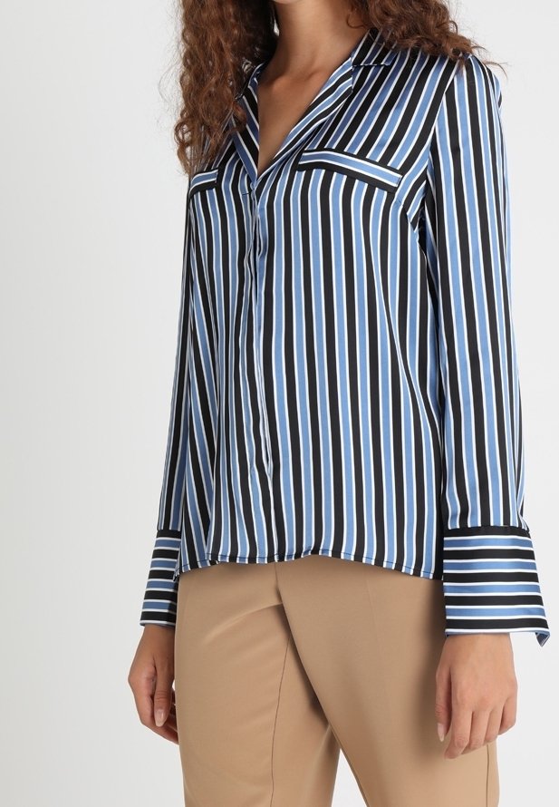 Blusa a righe blu, nera e bianca. Presenta un colletto, taschino frontale e maniche lunghe con polsini. Tessuto liscio, vestibilità comoda.