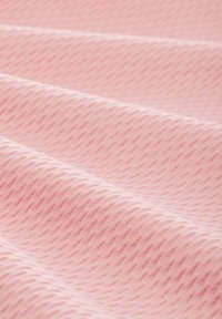 Ljusrosa strukturerad tyg med ett diagonalt diamantmönster, som har mjuka, släta veck och en något upphöjd yta.