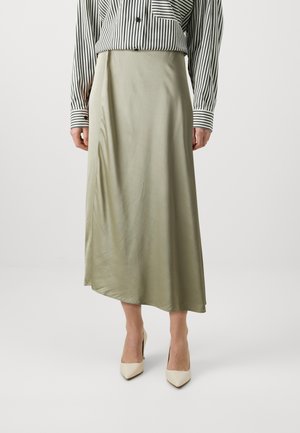 Satin grønn midiskjørt med en flytende silhuett. Har en lett asymmetrisk hemline og en glatt tekstur. Kombinert med kremfargede høye hæler.