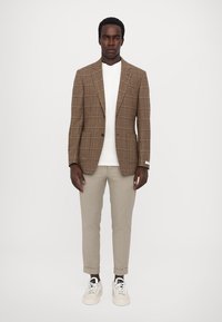 Brown checked blazer over a white t-shirt, paired with light beige tapered trousers and white sneakers. Simple and contemporary design.