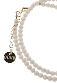 Kralenarmband gemaakt van witte, facettenkralen met een goudkleurige sluiting en een ronde hanger gegraveerd met "OTAZU."