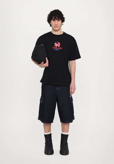 T-shirt noir avec un graphique coloré et un texte, associé à un short en denim cargo avec des poches latérales, et des bottines noires.