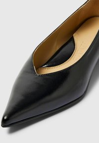 Ballerines noires en cuir avec un bout pointu et une découpe arrondie sur le côté, finition lisse. L'intérieur est doté d'une doublure beige.
