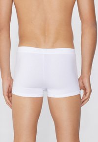 Boxers de algodón blancos con una cinturilla suave, diseño ajustado y textura lisa, vistos desde atrás, destacando las aberturas para las piernas.