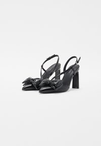 Escarpins noirs à talon slingback, à bout pointu, avec un grand nœud décoratif à l'avant. Texture en cuir lisse, talon bloc épais, bride de cheville réglable.