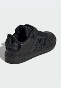 Black synthetic sneaker with a smooth finish, includes a strap closure, three tonal stripes, and embossed character details on the heel.