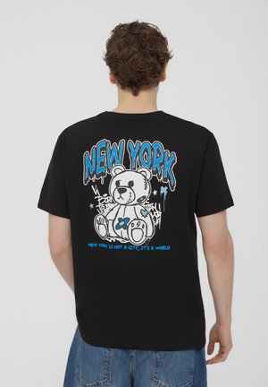 T-shirt nera in cotone con una grafica colorata di un orso e la scritta "NEW YORK" con elementi di graffiti sul retro. Maniche corte, vestibilità comoda.