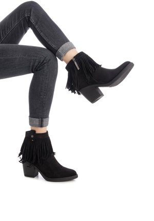 Stivaletti neri in suede alla caviglia con dettagli in frange, una cerniera laterale e un tacco a blocco testurizzato, abbinati a jeans scuri risvoltati.