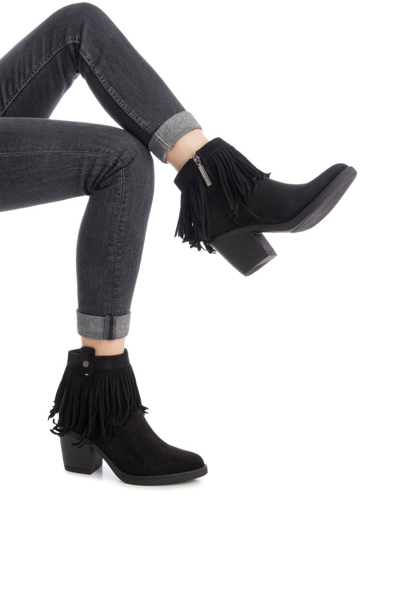 Stivaletti neri in suede alla caviglia con dettagli in frange, una cerniera laterale e un tacco a blocco testurizzato, abbinati a jeans scuri risvoltati.