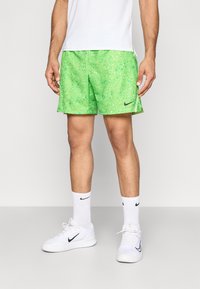 Πράσινα σορτς με σχέδιο που μοιάζει με στίγματα, φτιαγμένα από ελαφρύ υλικό. Συνδυασμένα με λευκές κάλτσες και παπούτσια Nike.