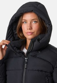 Svart pufferjacka med stor huva, dragkedjestängning och synlig söm. Slät textur och lätt isolering.