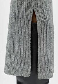 Tissu tricoté argenté avec un motif texturé, comportant une fente verticale en bas, superposé à un matériau noir lisse.