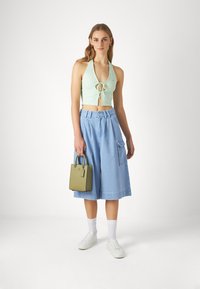 Mint green ribbed crop top with tie front, paired with light blue wide-leg denim shorts. Holding a small olive green handbag. White sneakers.