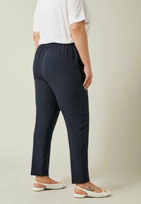 Marinblå elastiska midjebyxor med tapered passform, mjukt material och enfärgad design. Kombineras med vita slingback-skor.