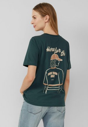 T-shirt en coton vert foncé à manches courtes avec un design imprimé d'une personne portant une casquette, texte de slogan, et une coupe décontractée.