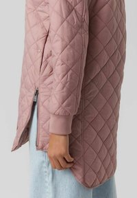Giubbotto trapuntato in morbido tessuto rosa con zip laterale e polsini in costina, caratterizzato da una silhouette lunga e una texture a motivo a rombi.