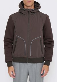 Giacca marrone con cappuccio, caratterizzata da un materiale esterno liscio, maniche scure a contrasto, tasche con cerniera e linee accentate di colore azzurro.