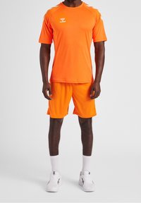 Camiseta deportiva naranja y pantalones cortos, hechos de tejido ligero. Cuenta con detalles blancos en los hombros y un diseño de cuello redondo estándar.