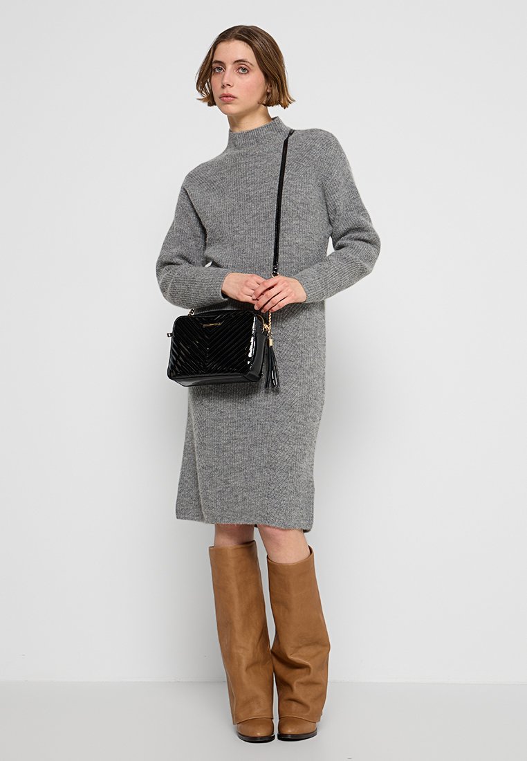 Robe en tricot grise à manches longues et col montant, associée à des bottes marron jusqu'aux genoux et un sac à main noir matelassé. Les textures lisses dominent.