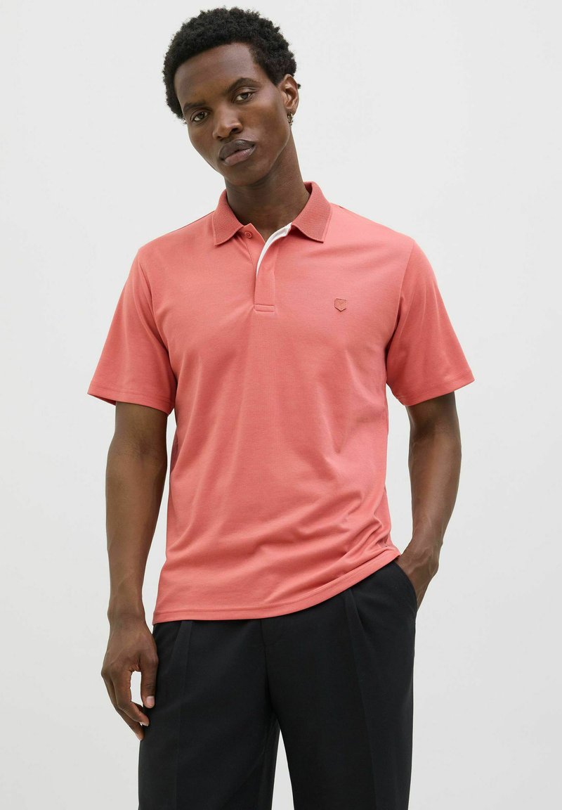 Rövid ujjú korall póló, kontrasztos fehér gallérral és egy diszkrét logóval a mellkasán. Simakészségű anyagból készült, klasszikus fazonban.