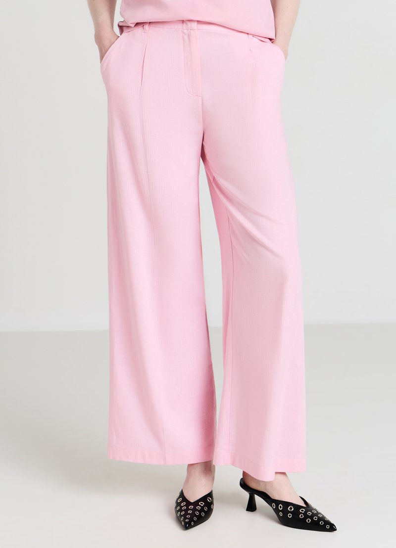 Pantalon à jambes larges en tissu rose doux à la texture lisse, doté de poches latérales et d'une ceinture ajustée.