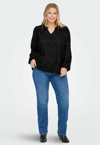 Blusa nera a maniche lunghe con scollatura a V e motivo testurizzato. Abbinata a jeans denim blu e stivaletti neri.