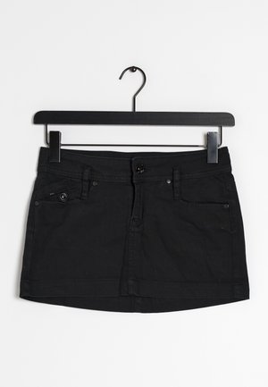 Jupe mini en denim noir suspendue à un cintre noir. Présente une fermeture à bouton devant, deux poches avant et une finition texturée.