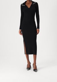 Svart ribbad knitklänning med krage som har pärlprydnader, lång ärm, figurnära silhuett och en sidoklyvning. Bärs med svarta klackar.