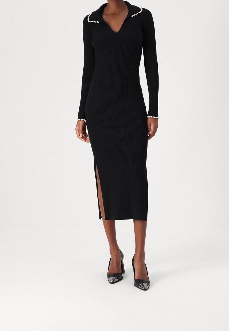 Svart ribbad knitklänning med krage som har pärlprydnader, lång ärm, figurnära silhuett och en sidoklyvning. Bärs med svarta klackar.