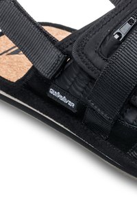 Sandalo nero con cinturini in tessuto e soletta in sughero. Dettagli notevoli includono un logo Quiksilver e una soletta testurizzata per una migliore aderenza.