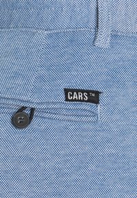 Světle modrá denimová tkanina s rybí kostrou, opatřená černou etiketou označenou "CARS™" a černým plastovým knoflíkovým zapínáním.