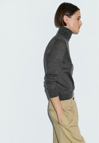 Maglione grigio a collo alto realizzato in morbido tessuto a maglia, abbinato a pantaloni beige chiaro. Il maglione ha maniche lunghe e un design aderente.
