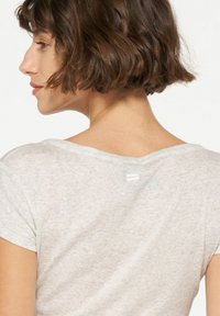 Lichtgrijze T-shirt met korte mouwen, voorzien van een brede halslijn en een klein rechthoekig label aan de achterkant, gemaakt van zachte, gestructureerde stof.