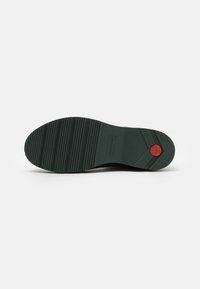Green rubber shoe sole with textured grip pattern and red emblem. Sturdy construction with a rounded shape and defined tread lines.