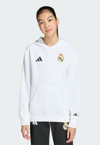Sweat à capuche blanc avec cordon de serrage, arborant un emblème Real Madrid doré et bleu ainsi qu'un logo Adidas noir. Poche kangourou et poignets côtelés.