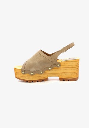 Sabots en suède beige à plateforme avec un bord festonné, des clous dorés et une semelle en bois. Dotés d'une sangle arrière et d'une semelle texturée.