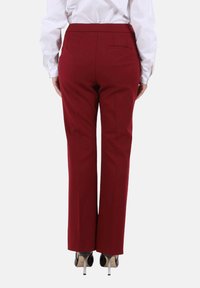 Pantaloni su misura color cremisi con design a gamba dritta, due tasche posteriori e tessuto liscio, abbinati a scarpe nere con tacco alto.