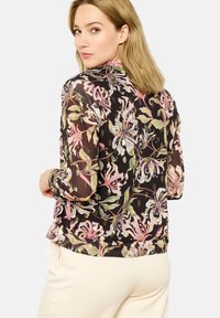 Floral blouse with long sheer sleeves in black, featuring pink and green flower patterns. Smooth texture and slightly loose fit.