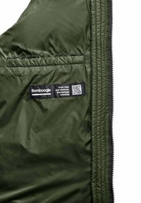 Olijfgroene nylon jas interieur met een zwart label met daarop een QR-code en tekst. Gladde textuur en een ritszak aan de linkerzijde.