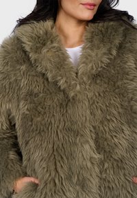 Olive green faux fur coat with a shaggy texture, wide lapels, and front pockets. Features a soft inner lining and a relaxed fit.