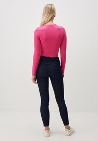 Maglietta aderente rosa a maniche lunghe con scollo rotondo, abbinata a jeans skinny in denim scuro a vita alta e sneakers bianche.